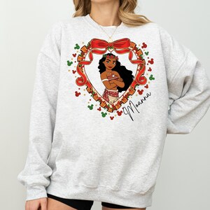 A woman wearing a gray sweatshirt with a heart-shaped graphic featuring a cartoon character and a bow.