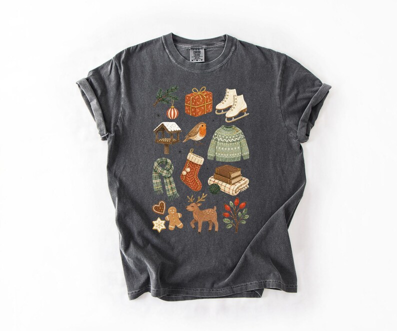 A gray t-shirt with a collage of various Christmas-themed items and decorations, including a pair of skis, a gift box, a Santa hat, a reindeer, a gingerbread man, and other festive symbols.