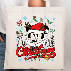 Puede incluir: Bolso tote color crema con Minnie Mouse con gorro de Pap&aacute; Noel y cuernos de reno. El dise&ntilde;o incluye la palabra "Christmas" en rojo, bastones de caramelo, copos de nieve y una guirnalda de luces.