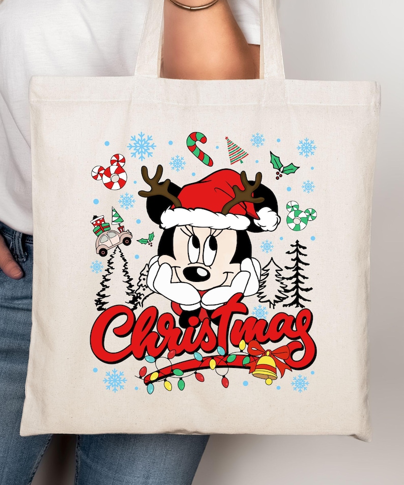 Puede incluir: Bolso tote color crema con Minnie Mouse con gorro de Pap&aacute; Noel y cuernos de reno. El dise&ntilde;o incluye la palabra "Christmas" en rojo, bastones de caramelo, copos de nieve y una guirnalda de luces.