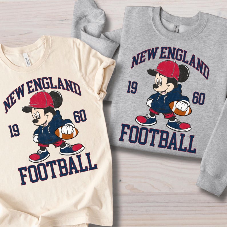May include: Two t-shirts featuring a cartoon Mickey Mouse in a football uniform. The shirts are cream and gray, with the text "NEW ENGLAND FOOTBALL 1960". Mickey is wearing a red cap, blue hoodie, and holding a football.