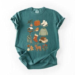 A green t-shirt with a collage of various Christmas-themed items and decorations, including a pair of skis, a gift box, a gingerbread man, a reindeer, and other festive symbols.