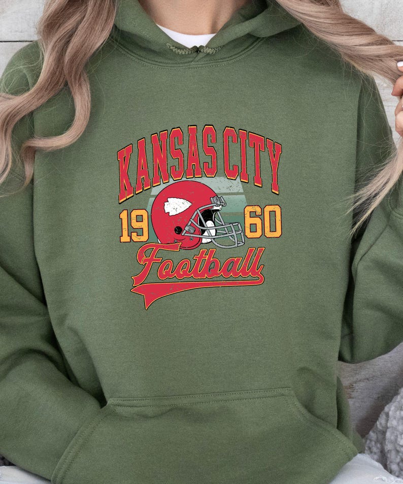 K&ouml;nnte beinhalten: Gr&uuml;ner Kapuzenpullover mit einem Vintage-Grafikdesign mit dem Text "Kansas City Football" mit einem roten Footballhelm und den Zahlen 19 und 60.