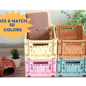 May include: Three stackable plastic storage crates in different colors: beige, pink, and blue. The crates have a grid pattern and are labeled "Mix & Match 50 Colors".