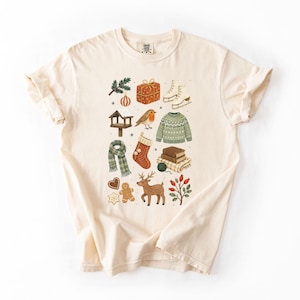 A white t-shirt with a graphic design featuring various Christmas-themed items such as a snowman, presents, a gingerbread man, and a reindeer.