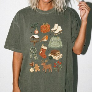 A person wearing a green t-shirt with a collage of various Christmas-themed illustrations, including a snowman, presents, skis, a bird, a reindeer, and other festive elements.