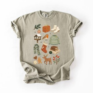 A t-shirt with a graphic design featuring various winter-themed items such as a snowman, Christmas tree, gift box, and other festive decorations.