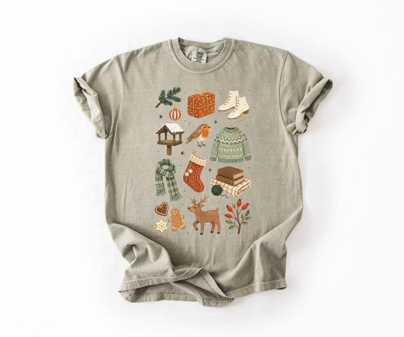 A t-shirt with a graphic design featuring various winter-themed items such as a snowman, Christmas tree, gift box, and other festive decorations.