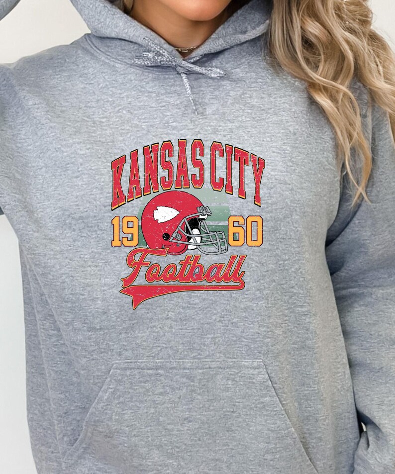 K&ouml;nnte beinhalten: Grauer Kapuzenpullover mit einem Vintage-Grafikdruck eines Footballhelms und dem Text "Kansas City 1960 Football".