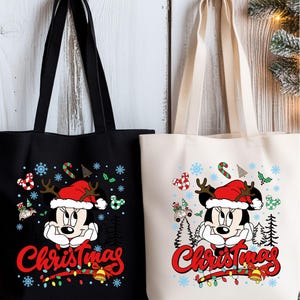 Puede incluir: Dos bolsas de mano, una negra y otra blanquecina, presentan un dise&ntilde;o de Minnie Mouse con tem&aacute;tica navide&ntilde;a. El dise&ntilde;o incluye copos de nieve, bastones de caramelo y la palabra "Christmas" en escritura roja. Las bolsas tienen asas negras.