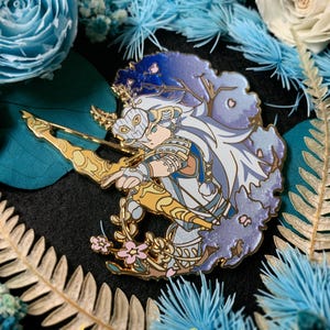 May include: A detailed enamel pin featuring a character with a bow and arrow, set against a backdrop of blue and purple hues. The pin has gold accents and is surrounded by floral and botanical elements. The design is intricate and artistic.