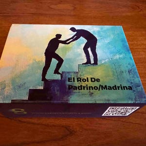 May include: Box with a colorful abstract design featuring two silhouetted figures, one helping the other climb stairs. Text on the box reads "El Rol De Padrino/Madrina". The background has blue, green, and yellow hues.