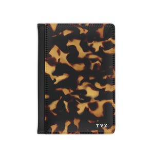 May include: A black leather passport holder with a tortoiseshell pattern and the initials "TVZ" embossed in white.
