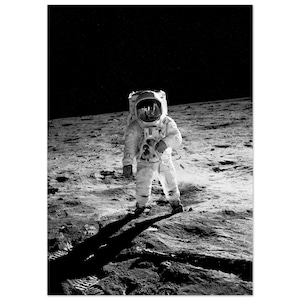 Pode incluir: Uma fotografia a preto e branco de um astronauta de pé na superfície da lua. O astronauta está a usar um fato espacial branco com um capacete e está a olhar para a câmara.