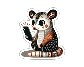 Könnte beinhalten: Ein Aufkleber mit einem Cartoon-Opossum, das ein Smartphone hält. Das Opossum hat ein weißes Gesicht, braunes und schwarzes Fell und einen gestreiften Schwanz. Das Telefon ist schwarz und das Design hat einen weißen Rand.