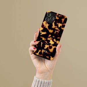 Op de afbeelding: Een bruine en zwarte schildpad-telefoonhoes met een gouden logo met de tekst "TVZ".