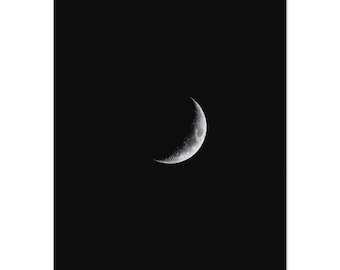 May include: A monochrome image of a crescent moon set against a black backdrop. The moon is a bright white, showing surface details. The photograph is high-contrast, creating a dramatic effect, reminiscent of the night sky.