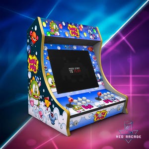 Puede incluir: Una colorida máquina recreativa con personajes y gráficos del juego Bubble Bobble. La máquina tiene una pantalla grande que muestra "Press Start to Play". Incluye joysticks, botones y el logotipo de Taito. La máquina es blanca, azul y dorada.