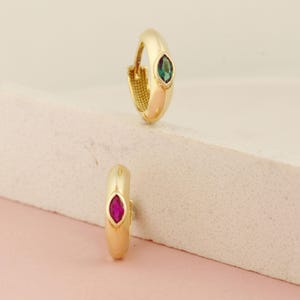 May include: Two gold hoop earrings with a single emerald green and ruby red gemstone set in each hoop.
