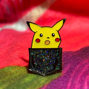 Puede incluir: Un pin de esmalte negro que representa a un personaje de dibujos animados Pikachu amarillo con una expresión de sorpresa. El pin presenta un bolsillo negro brillante con un contorno plateado.