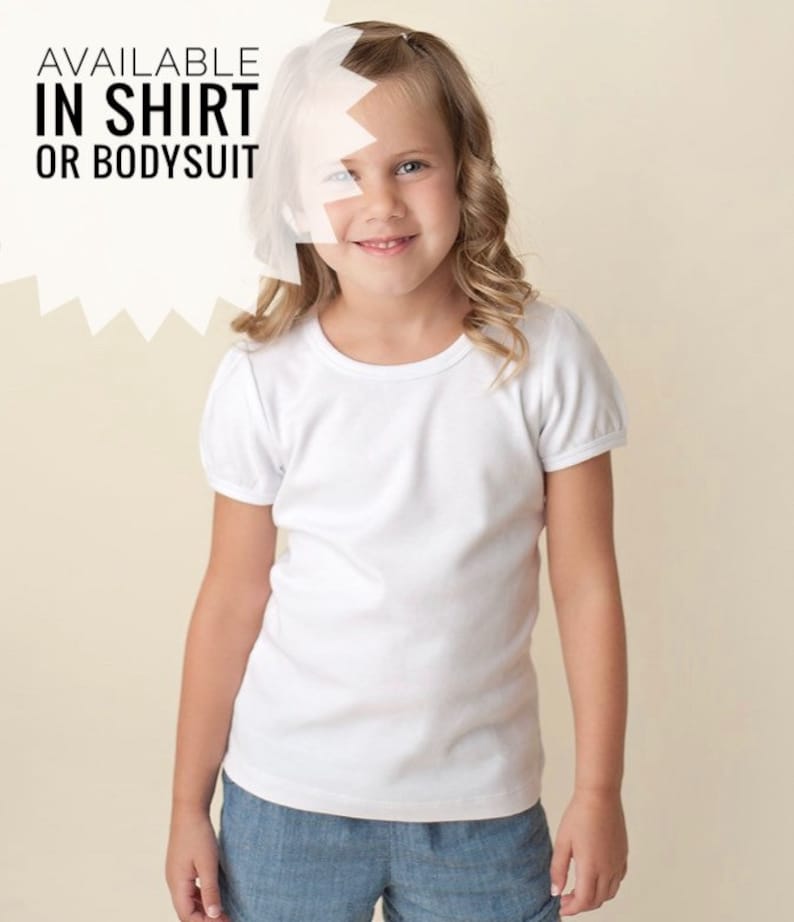 May include: A young girl wearing a white short-sleeved t-shirt and blue denim shorts. The text "AVAILABLE IN SHIRT OR BODYSUIT" is visible in the image.