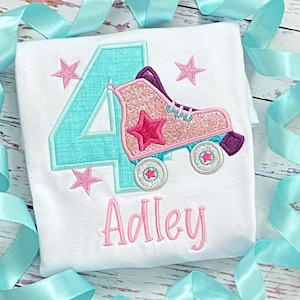 Pu&ograve; includere: Una maglietta bianca con un numero quattro turchese e un pattino rosa con una stella rosa. Il nome "Adley" &egrave; scritto in rosa sotto il pattino.