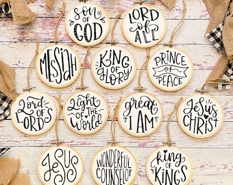 May include: Twelve white round ornaments with black lettering. Each ornament has a different phrase related to Jesus Christ, such as "Son of God", "King of Glory", and "Jesus Christ".