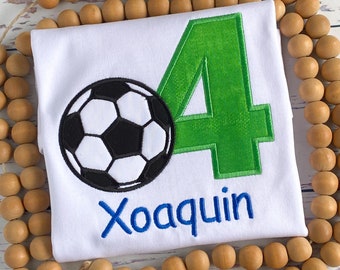 May include: White t-shirt with a green number 4, a black and white soccer ball, and the name "Joaquin" in blue embroidery.