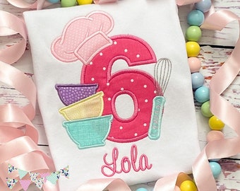 May include: Pink and white polka dot number six with a pink chef's hat, a set of colorful mixing bowls, and a whisk. The name Lola is embroidered below the number.