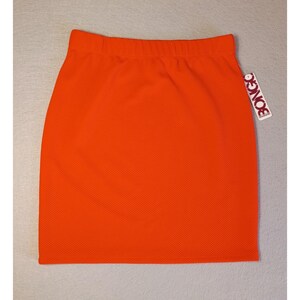 May include: Bright orange mini skirt with an elastic waistband. The skirt has a textured surface and a tag that reads "BONGO". The skirt is a solid color and appears to be made of a knit fabric.