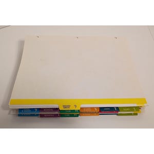 May include: A stack of white paper sheets with a yellow bottom border and multi-colored index tabs labeled with numbers and categories including Gifts, Baby, Toys & Dolls, Misc, Fashion Accessories, and Quick & Easy. The paper has three holes.
