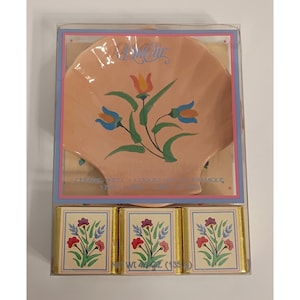 May include: A ceramic shell-shaped dish with a floral design in a clear plastic box. The dish is peach-colored with a painted floral design in blue, red, and green. Below the dish are three small, wrapped bars with matching floral designs. The net weight is 4 oz (113 g).