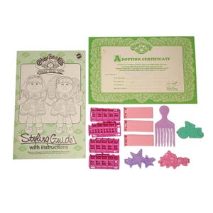 May include: A vintage Cabbage Patch Kids Styling Hair Kid set. Includes a styling guide, adoption certificate, pink curlers, barrettes, and a comb. The styling guide features illustrations of the dolls.