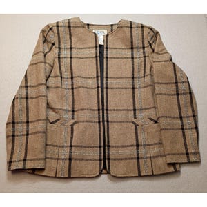 May include: A tan blazer with a plaid pattern in black and silver. The blazer has a round neckline, two front pockets, and a black lining. The label reads "BIDA".