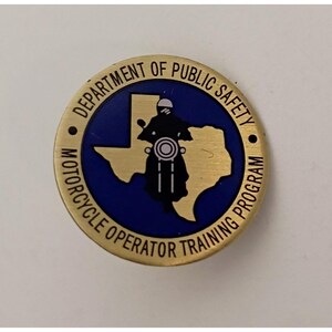 May include: A circular gold-toned metal pin featuring a blue center with a gold silhouette of the state of Texas. A black motorcycle and rider icon is centered on the state. The text reads DEPARTMENT OF PUBLIC SAFETY MOTORCYCLE OPERATOR TRAINING PROGRAM.