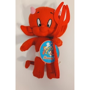 May include: A plush red devil doll with pink horns, a white diaper, and a red trident. The doll has black eyes and a tag with cartoon characters and the name "Harvey". A fun, collectible toy.