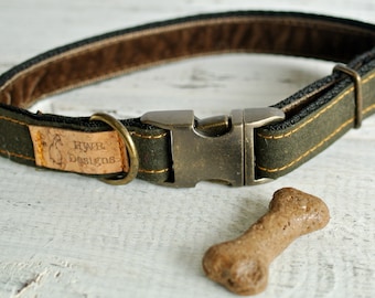 May include: A green canvas dog collar with brown leather trim and a brass buckle. The collar has a brown leather tag with the text "HYWB Designs" on it. A brown dog bone is lying on a white wooden surface.