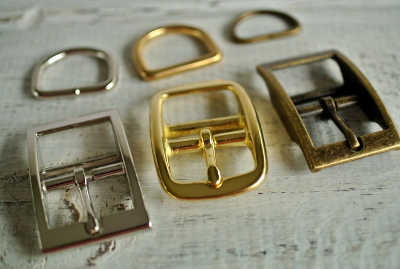 May include: Five different metal buckles in various sizes and finishes. The buckles are made of silver, gold, and brass. They are all rectangular in shape and have a simple design.