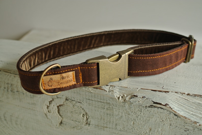 May include: A brown leather dog collar with a brass buckle and a small, rectangular tag that reads "HWR Designs".
