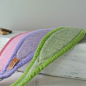 May include: Three dog collars made of tweed fabric with a herringbone pattern. The collars are in pink, purple, and green. The collars have a velvet trim and are lined with a soft, plush fabric. The collars are displayed on a white wooden surface.
