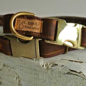 May include: A brown leather dog collar with a brass buckle and a cork tag that reads "HWR Designs".
