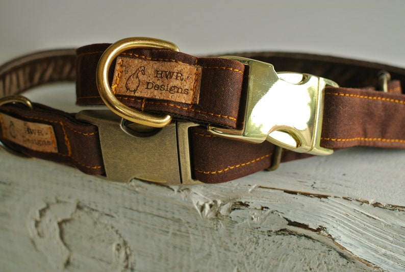 May include: A brown leather dog collar with a brass buckle and a cork tag that reads "HWR Designs".