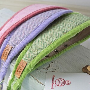 May include: Three dog collars in different colors: pink, lavender, and green. Each collar has a herringbone pattern and a contrasting colored velvet trim. The collars are made of tweed and have a leather label with the text "How's Tweed" on them.