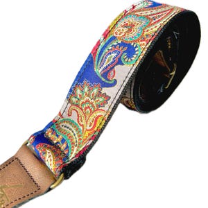 May include: A guitar strap featuring a vibrant paisley design in blue, red, yellow, and green. The strap has a leather end and a gold-coloured buckle.