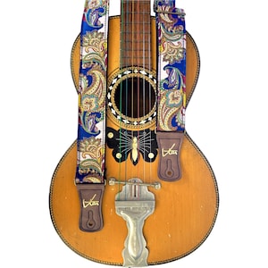 May include: An acoustic guitar with a blue paisley patterned guitar strap. The strap has brown leather ends with the word "Star" printed on them. The guitar features a butterfly design on the body.