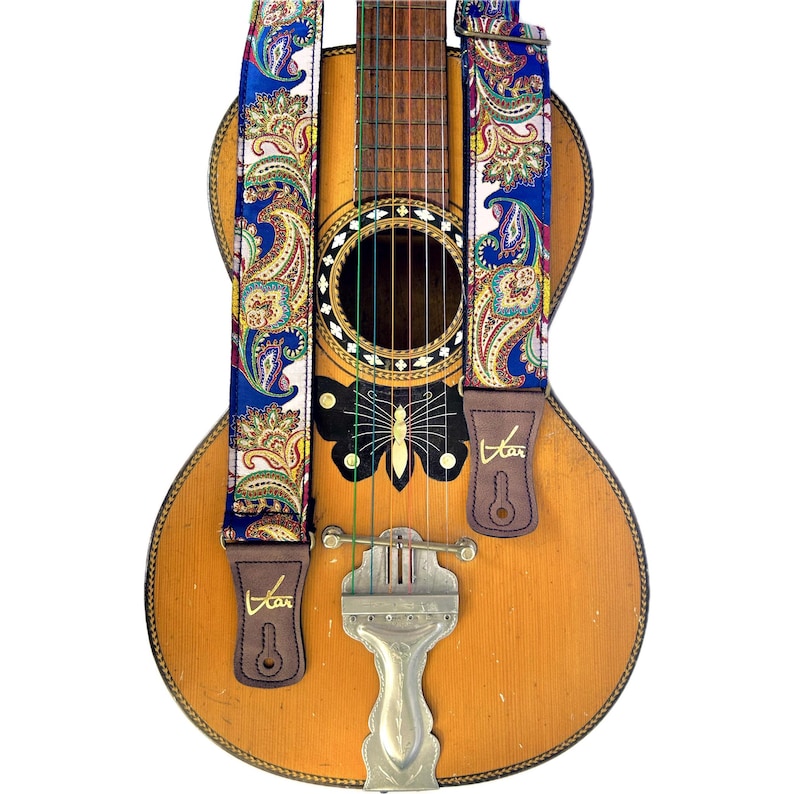 May include: An acoustic guitar with a blue paisley patterned guitar strap. The strap has brown leather ends with the word "Star" printed on them. The guitar features a butterfly design on the body.