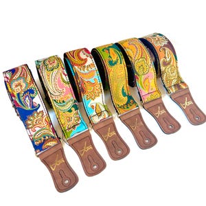May include: Six guitar straps with vibrant paisley designs in shades of blue, pink, green, and orange. Each strap features brown leather ends, with the word "Kar" printed in gold.