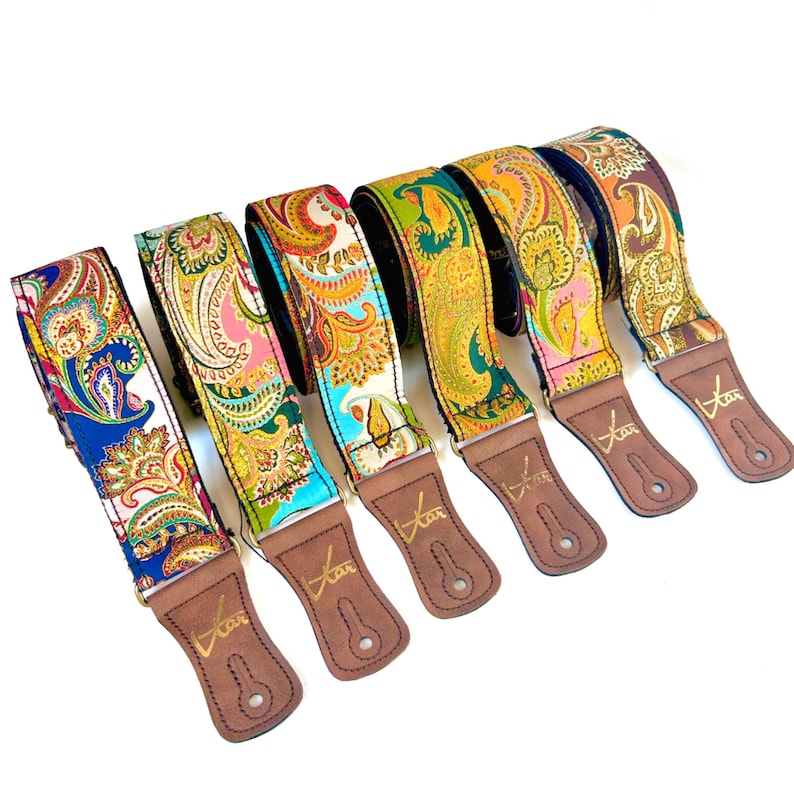 May include: Six guitar straps with vibrant paisley designs in shades of blue, pink, green, and orange. Each strap features brown leather ends, with the word "Kar" printed in gold.