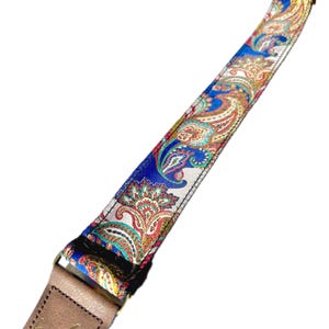 May include: A guitar strap featuring a vibrant paisley pattern in blue, red, yellow, and green. The strap has a leather end and metal hardware. The paisley design is a classic and eye-catching detail.