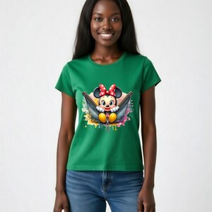 May include: Green t-shirt featuring a graphic of Minnie Mouse peeking out of a zipper. The cartoon character has a red bow and yellow shoes. The zipper is black with a gold-colored pull. The background has colorful paint splatters.